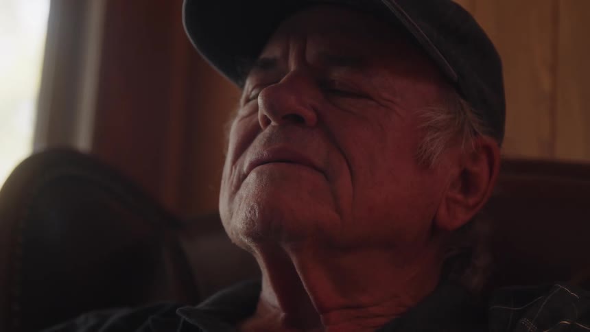 Portrait of an elderly man in a cap sitting and removing his glasses