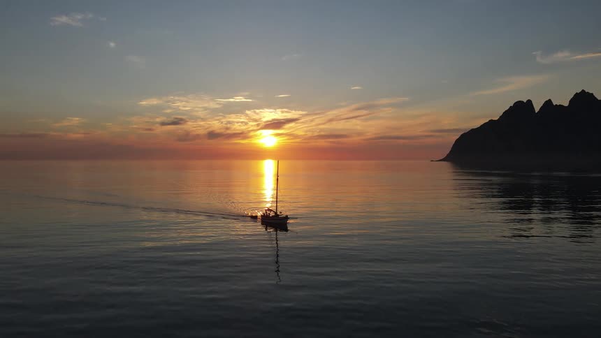 A boat sails off the coast as the sun sets on the horizon