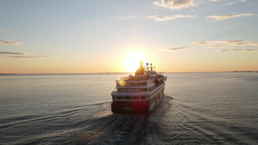 Cruise ship out at sea with sun shinning above the horizon reflecting off the water and a blue sky