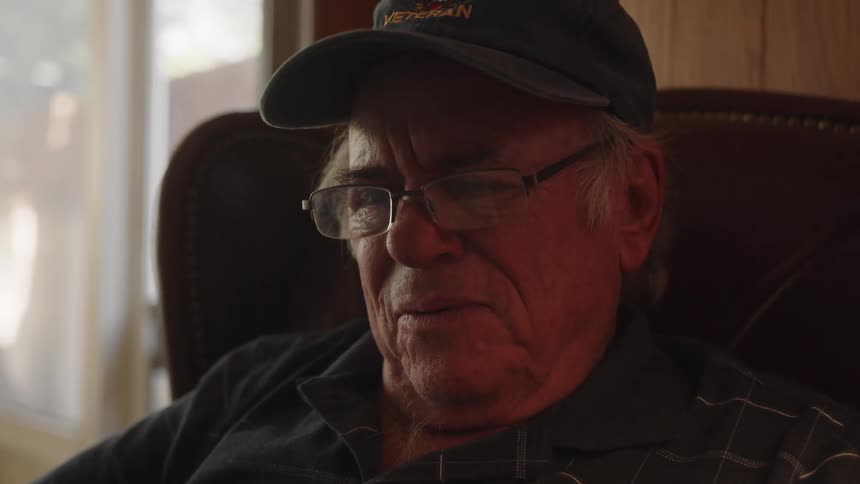 Elderly man sitting in armchair with glasses and cap reading newspaper