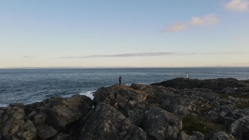 A person on the shore of the beach on a rocky mountain during sunset