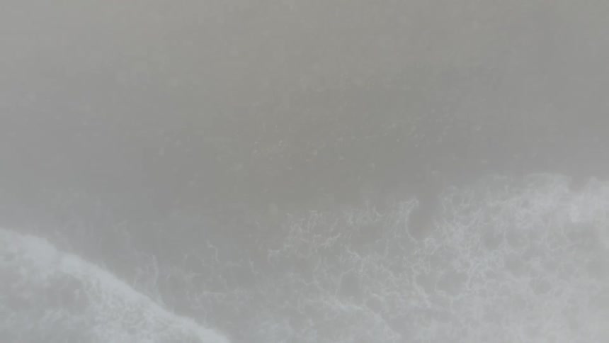 Top view of the beach with waves crashing against rocks on a foggy day