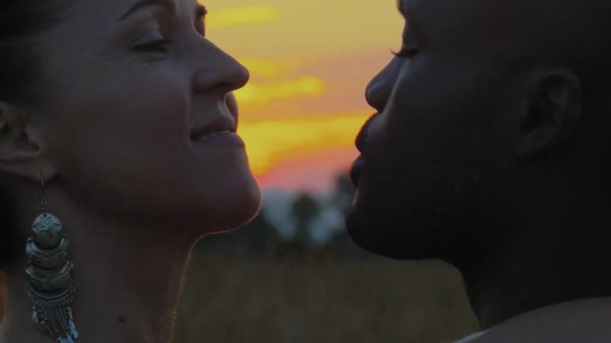 A man and woman kiss outside at sunset