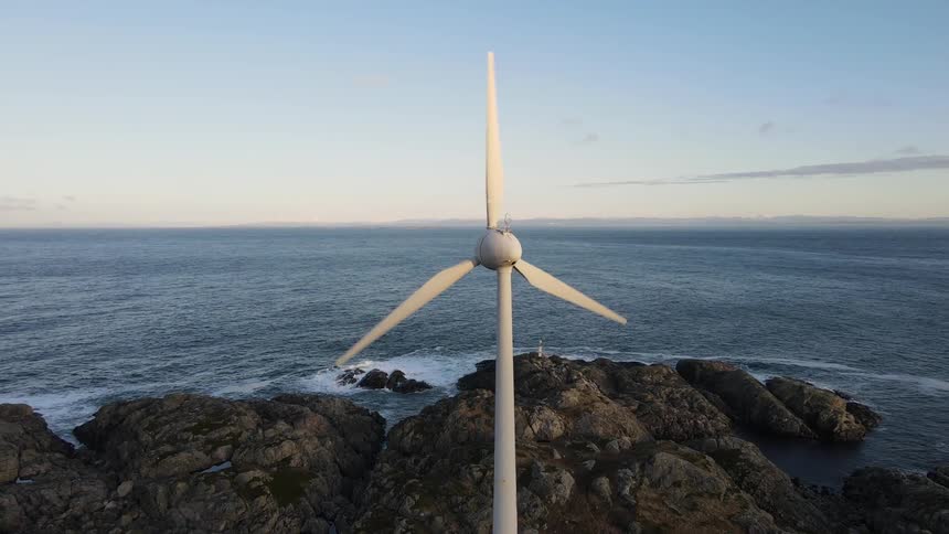 A wind turbine on the shore of a rocky beach