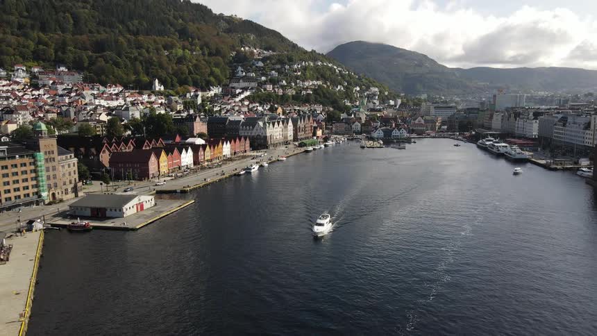 Aerial panorama of a boat passing under the sea along the shoreline of an urban city nestled between hills and mountains
