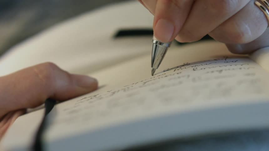 A person is writing in a small notebook