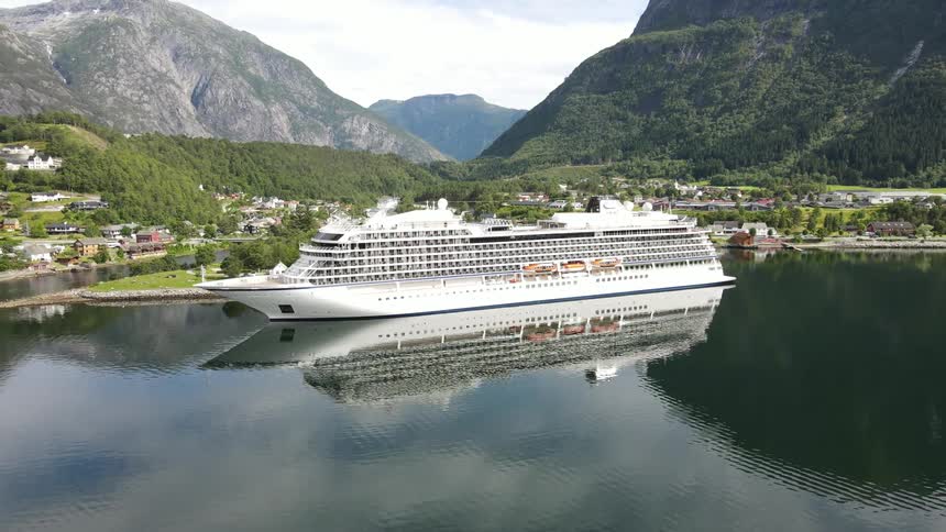 Aerial view of a cruise ship moored at sea next to a city amidst natural mountains
