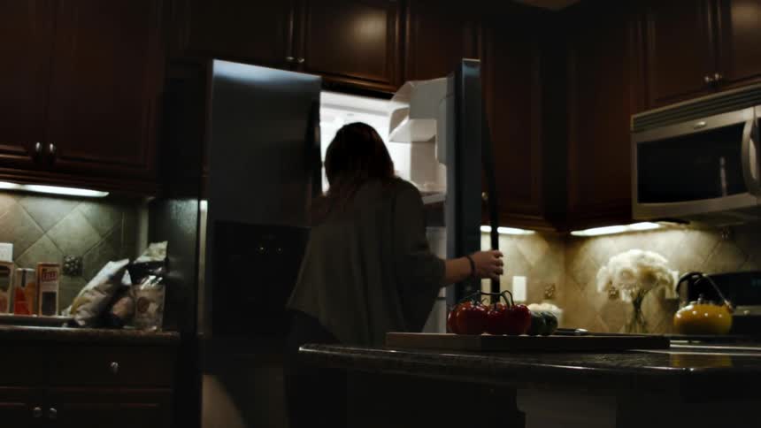 A woman removes some vegetables from the fridge