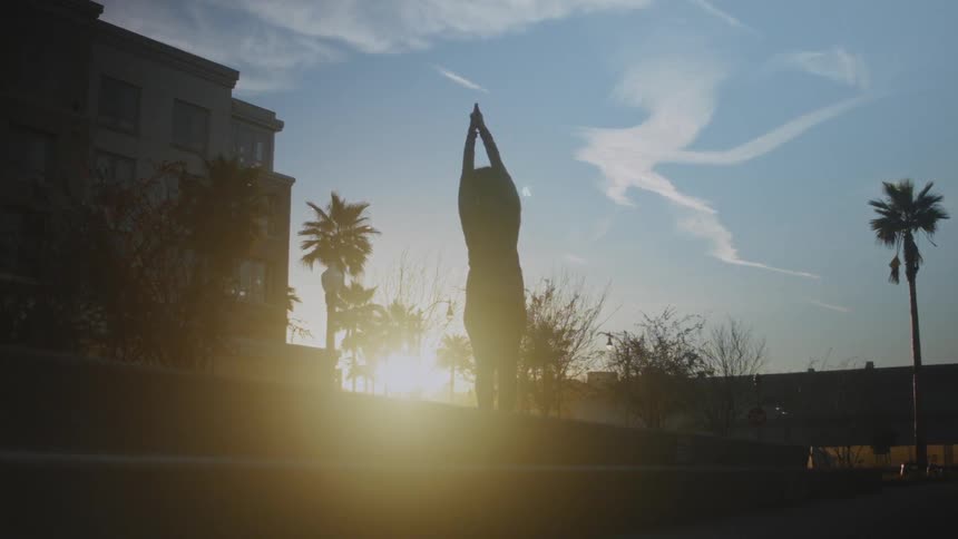 A woman is stretching by a building at sunrise