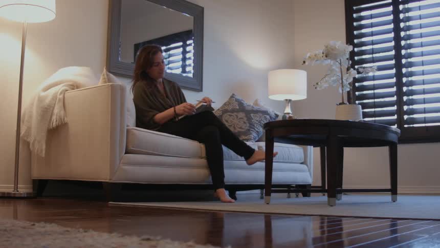 A woman walks over to the couch to write in a book