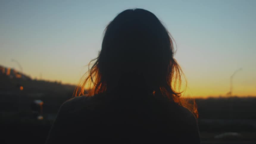 A woman watches the sun set in the distance