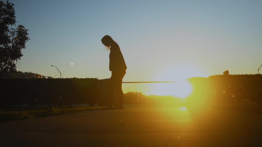Woman taking off sandals and walking onto grass at sunset