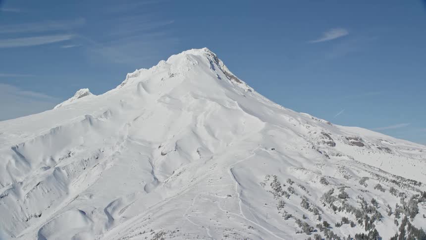 The sun shines upon a snow covered mountain with a peak high in the sky