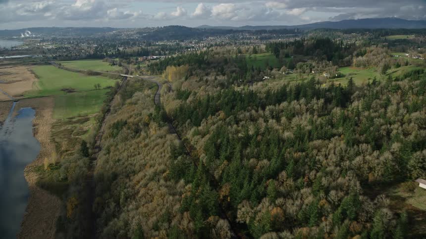 Aerial view of fields with forests lakes and a train track with an urban city in the background on the horizon