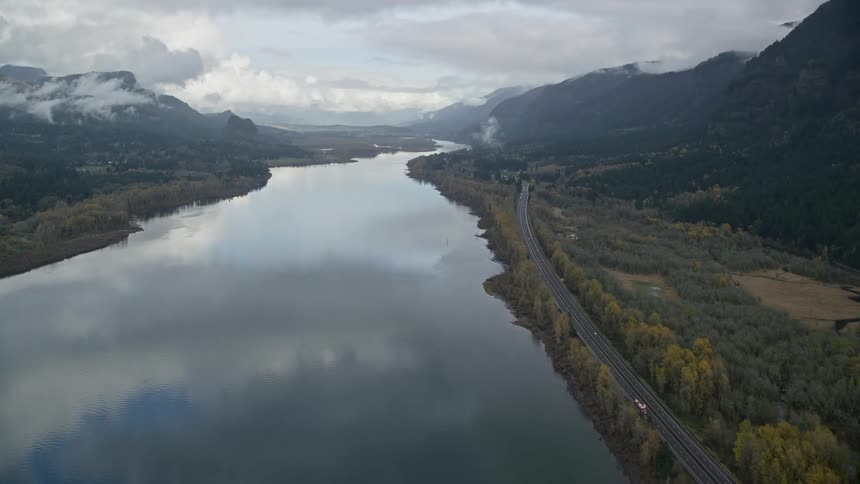 Aerial of a highway on the banks of a river surrounded by forest during sunset