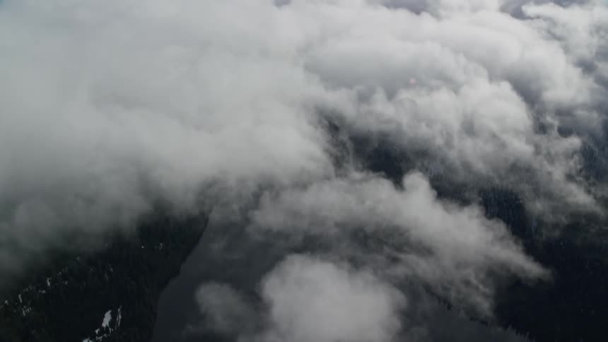Aerial of lake and forest covered by clouds in a glacial mountain landscape