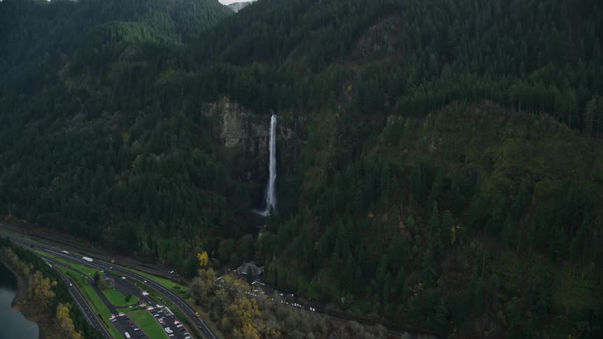 Aerial landscape of a road in the middle of a lake and next to mountains with a waterfall