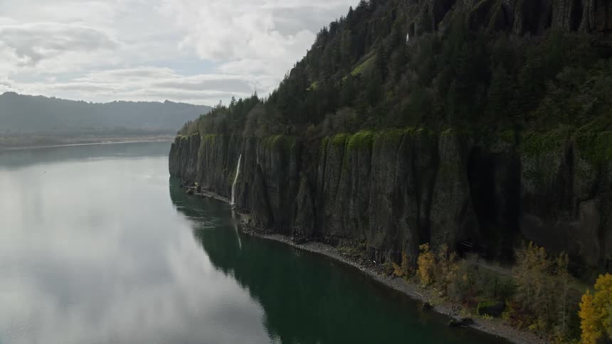 Panorama of a reflective lake with a mountain beside it featuring waterfalls and cascades