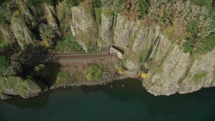 Train passing through a cave in a mountain beside a greenish lake