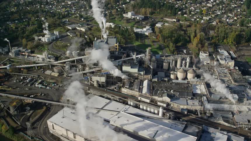 Aerial view of a factory releasing smoke into the air next to a small town