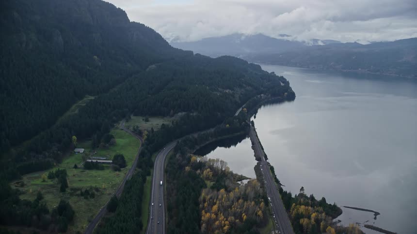 Aerial view of a road amidst a chain of mountains with forests and beside a lake