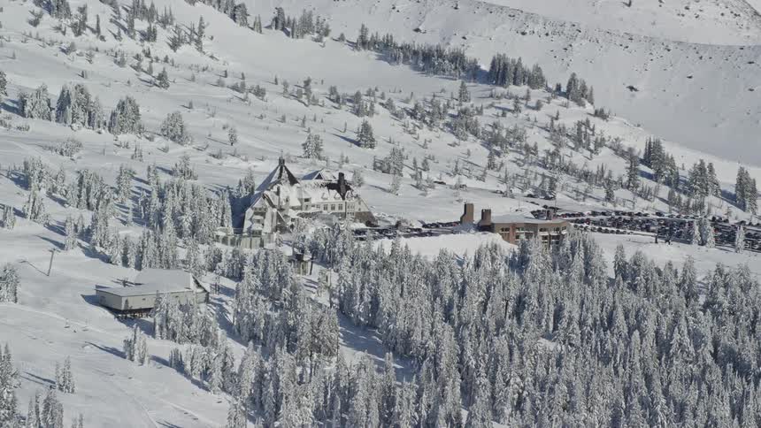 Aerial landscape of a house on a hill in the mountains with conifers around covered in snow