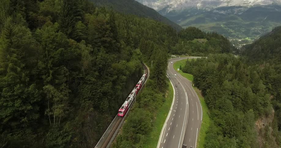 Train traveling near a highway surrounded by forest
