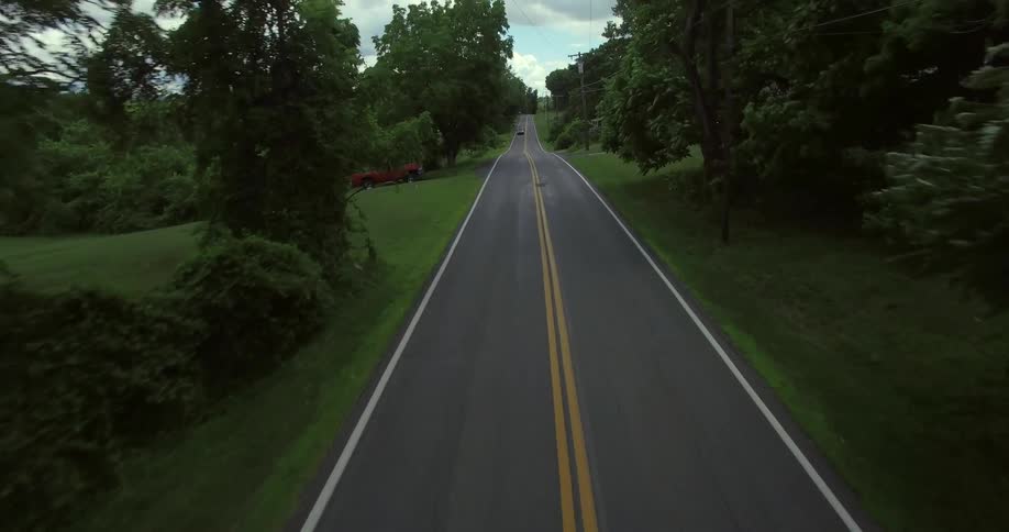 Moving down a road past a pickup truck parked on the grass