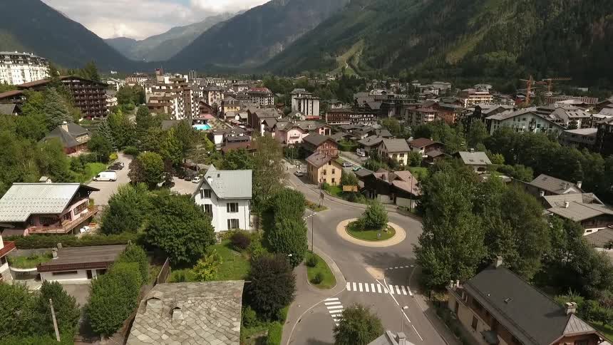 A town sits at the bottom of mountains with cars driving on the roads below