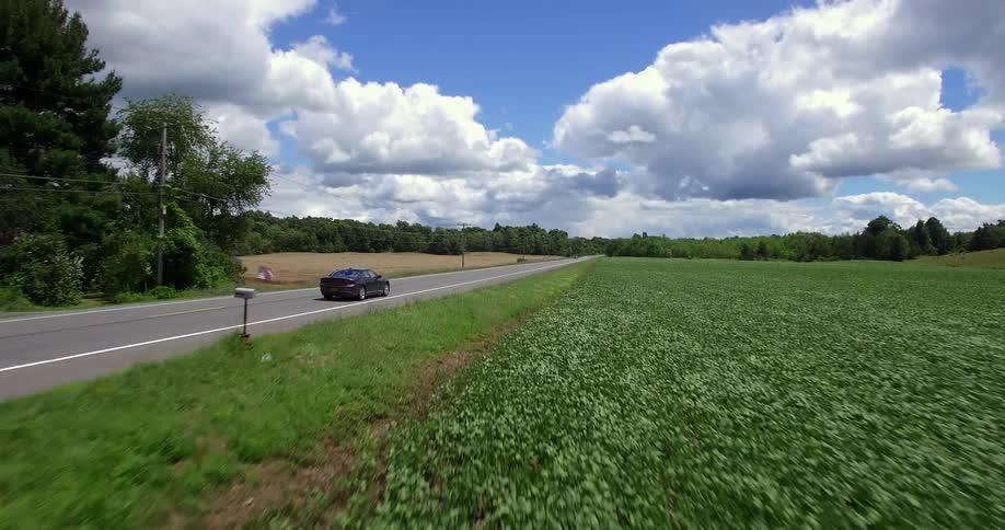 A black car drives down the road near a field