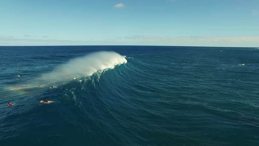 A wave passes by surfers causing a rainbow