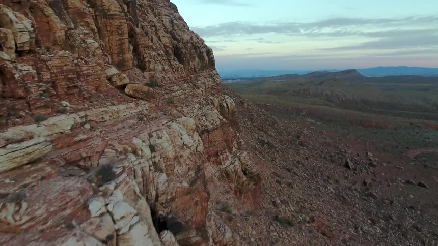 The striated rocks of a cliff with hills in the distance