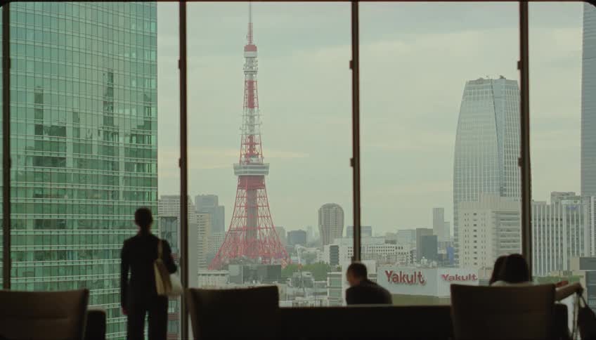 A woman watches the skyline from an airport window while three other people are sitting on airport chairs waiting for their flights