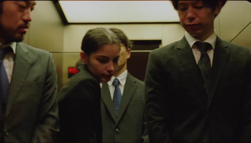 Elevator door opening and a woman stepping out surrounded by three men in suits