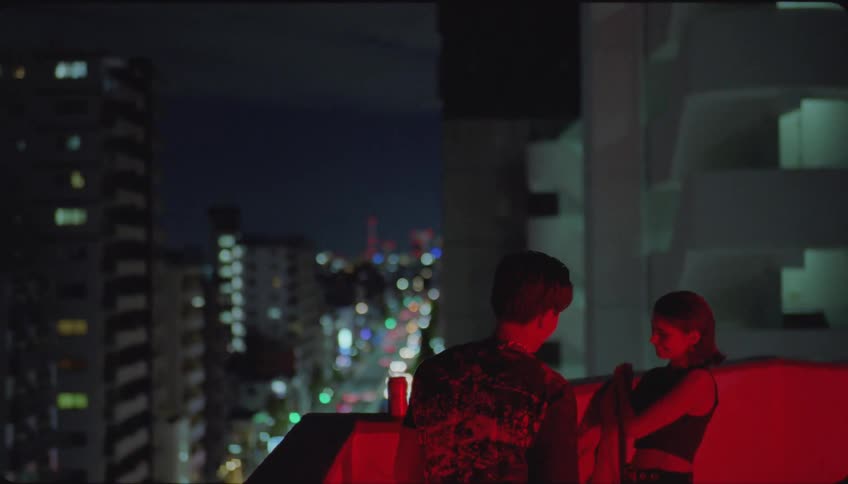 A man hands a woman his jacket on the balcony