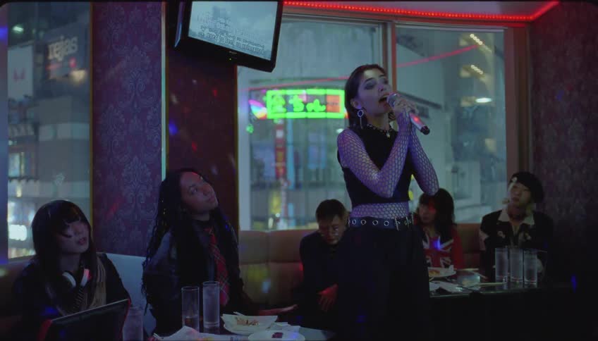 A young woman is singing and other women are sitting in a night club with lights