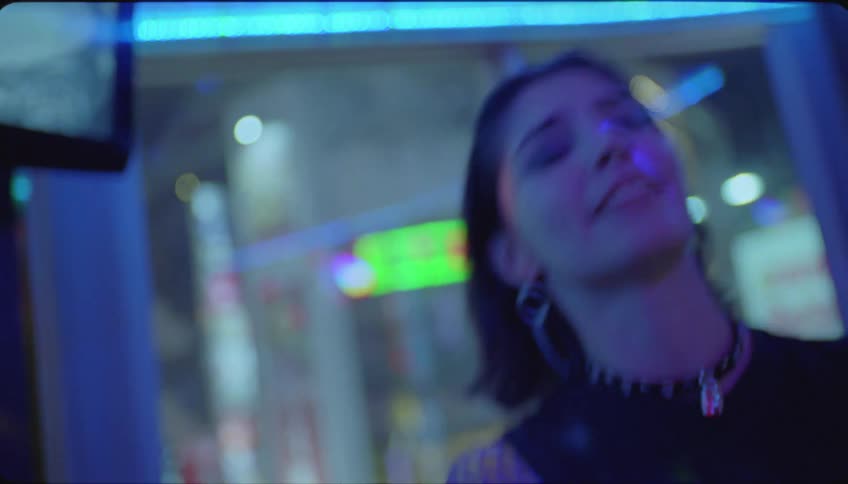 Young woman singing into a microphone at karaoke in a room illuminated by colorful led lights