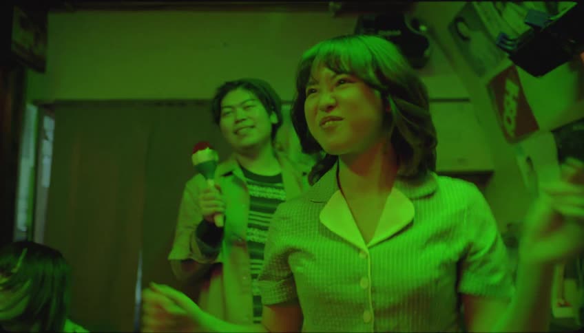 Friends sing and dance in room lit by greenish light