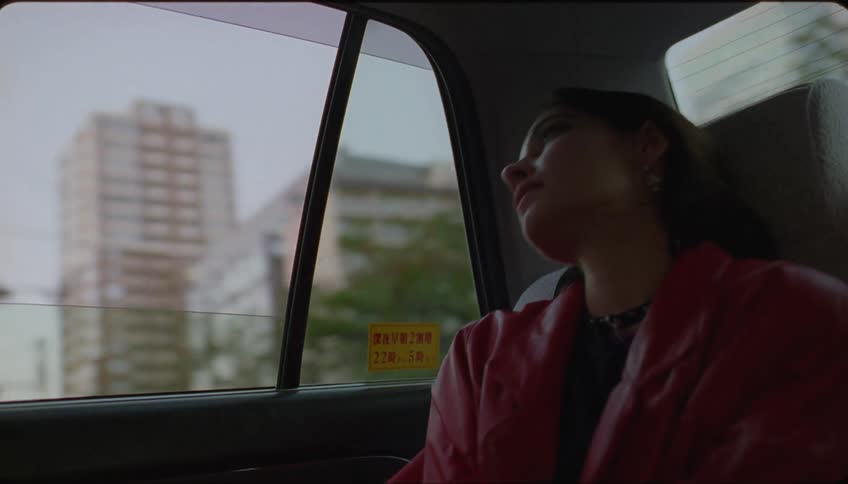 Woman waves goodbye from a moving car in the city