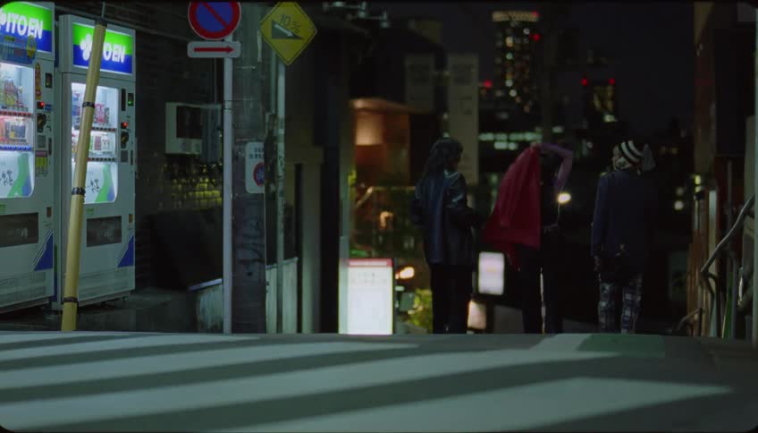 Friends walking on a street at night and one of them offers her red coat to another who puts it on