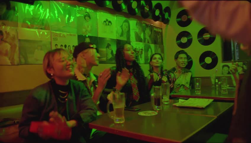 People in a pub with one of them singing karaoke and the others celebrating along