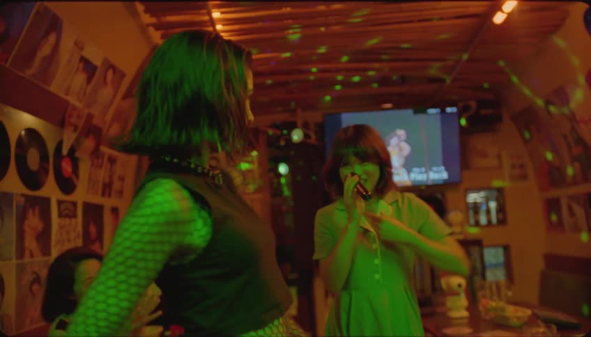 Friends inside a nightclub with one of them singing karaoke and the others dancing happily