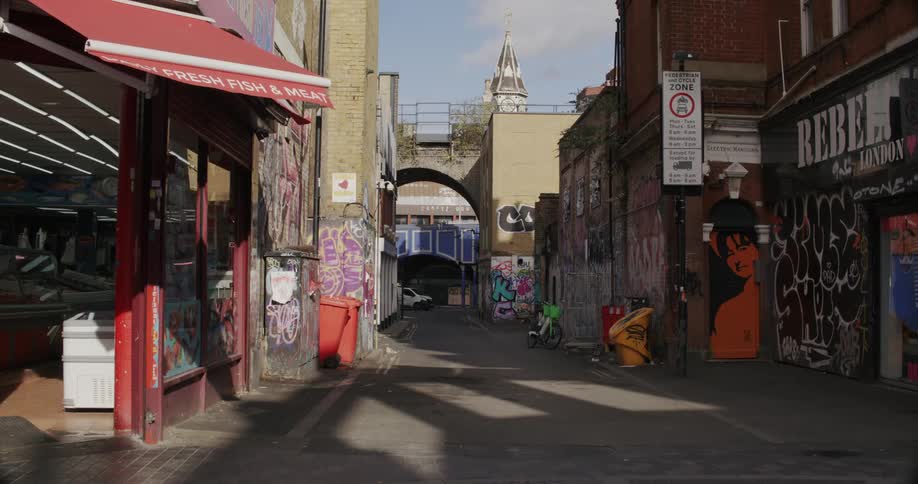 View of an alley in the middle of a city with a shop and graffiti on the walls