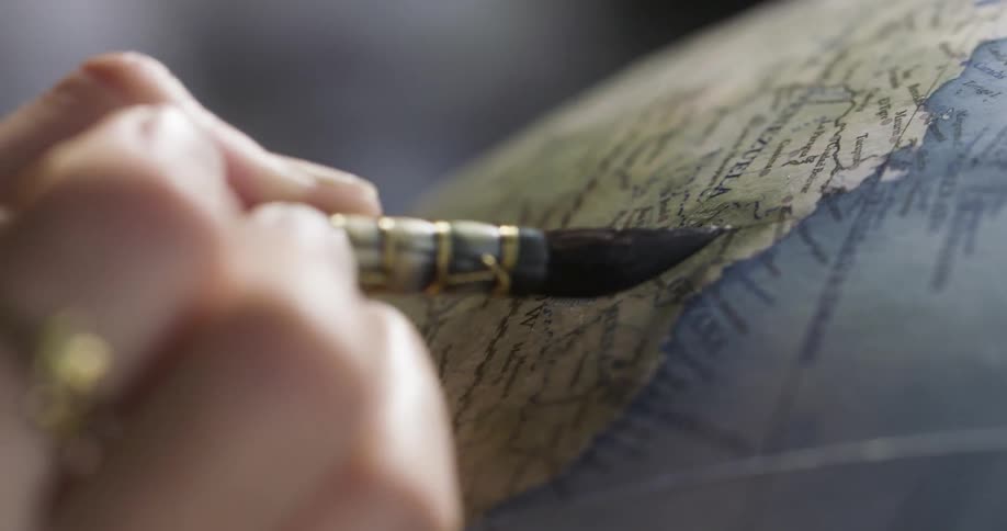 Extreme closeup of a persons hands painting a globe with a brush
