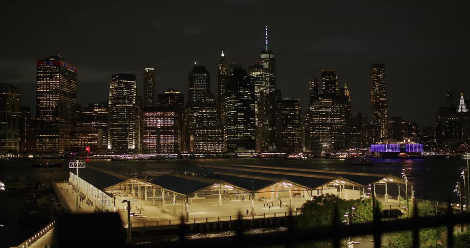 A landscape of illuminated skyscrapers and brooklyn bridge park at night