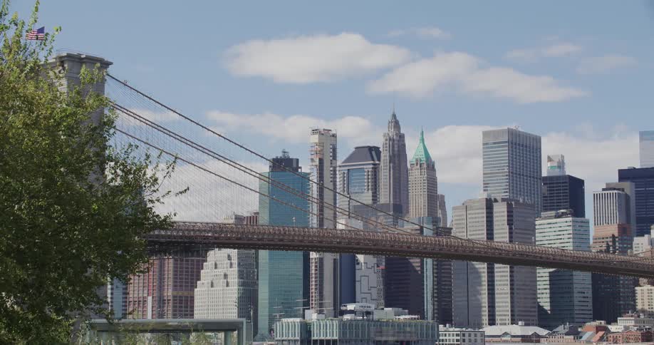 The new york city skyline stretches across the horizon with the brooklyn bridge standing prominently in the foreground