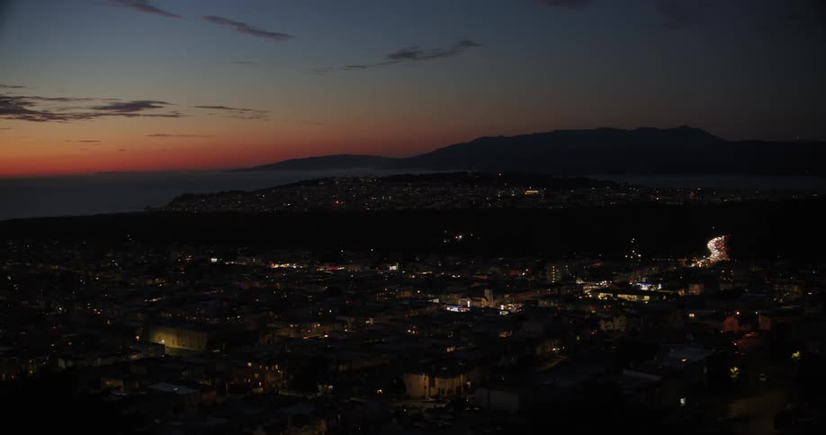 View of an urban city at night with a reddish evening sky and a chain of mountains on the horizon