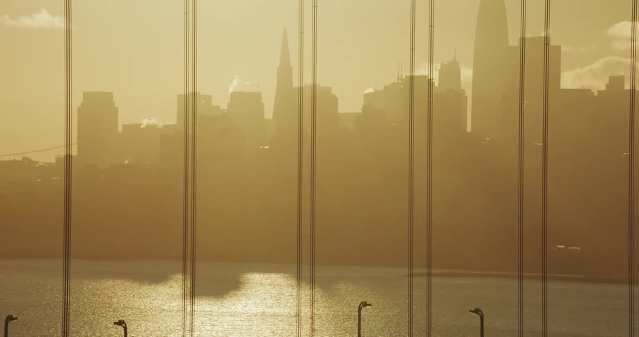 Cars crossing the golden gate bridge at sunset with city skyline in the background