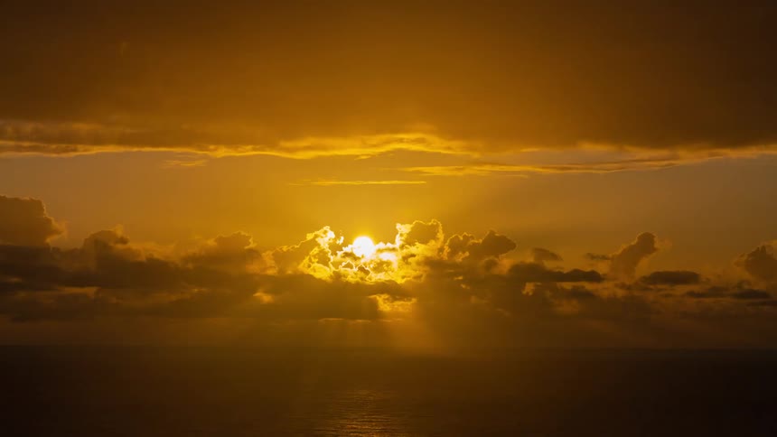 Clouds move over the water as the sun rises in an orange sky