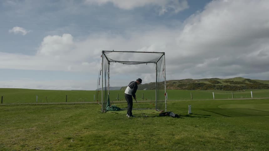 Man practices golf in front of a net on the golf course